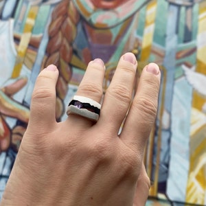 May include: A white ceramic ring with a black band and a purple stone inlay.