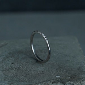 May include: A thin silver band with a row of small diamonds set in the metal.