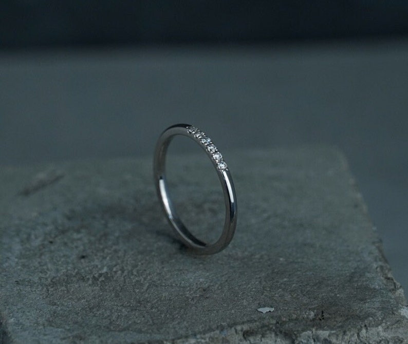 May include: A thin silver band with a row of small diamonds set in the metal.