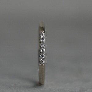May include: A thin silver band with a row of small diamonds set into the metal.