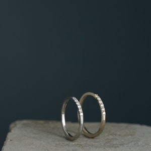 May include: Two thin wedding bands with small diamonds set in the band. The bands are on a gray concrete surface.
