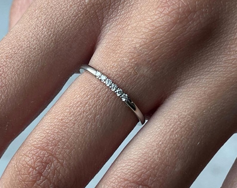 May include: A thin silver band ring with a row of small clear diamonds set in the center.