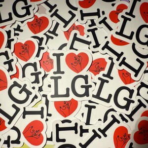 Op de afbeelding: Een verzameling witte stickers met de tekst "I LG" in zwarte letters, elk met een rood hart met een handillustratie. De stickers zijn verspreid, wat een visueel aantrekkelijk patroon cre&euml;ert.