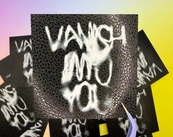 Op de afbeelding: Een vierkante zwarte sticker met een gestructureerd kunstlederen oppervlak met de witte, wazige tekst "VANISH INTO YOU" in een gestileerd handschrift. Een lichtpaarse pincet is zichtbaar in de rechterbenedenhoek van de sticker.