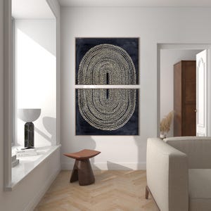 May include: Two framed abstract art prints. Each print features a dark navy background with a cream-colored dotted design forming a symmetrical arch shape. The prints are displayed above a brown wooden stool with a leather seat.
