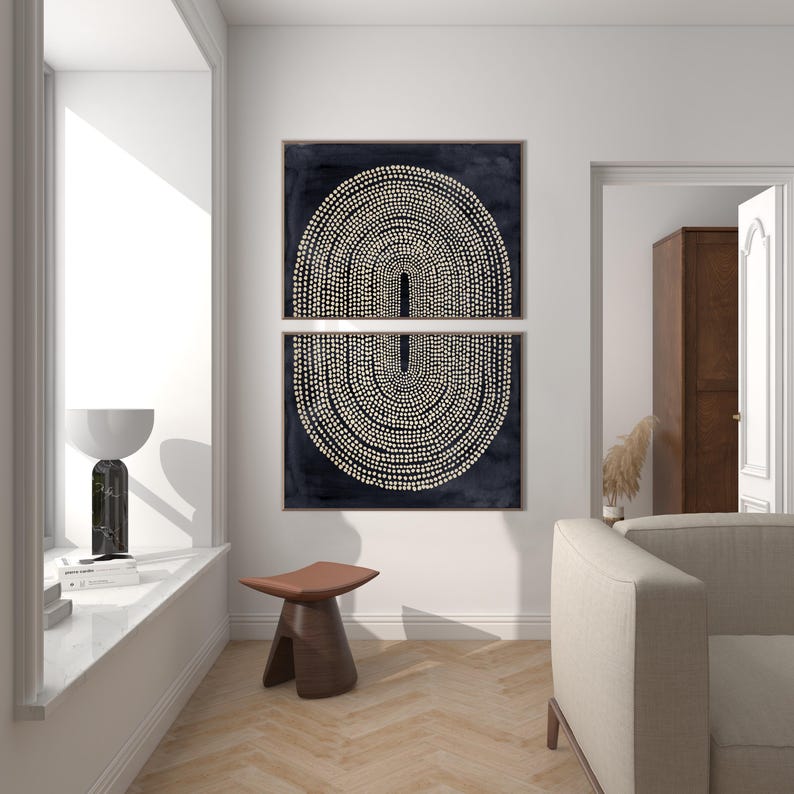 May include: Two framed abstract art prints. Each print features a dark navy background with a cream-colored dotted design forming a symmetrical arch shape. The prints are displayed above a brown wooden stool with a leather seat.