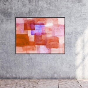 Peut inclure: Peinture abstraite &agrave; l'aquarelle dans un cadre noir. L'&oelig;uvre pr&eacute;sente des carr&eacute;s superpos&eacute;s dans des tons orange, rose et violet. La peinture est expos&eacute;e sur un mur gris au-dessus d'un sol en bois.