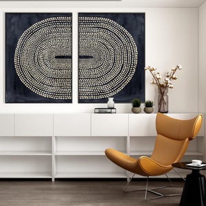 May include: Two abstract wall art pieces with a dark blue background and a pattern of white dots arranged in concentric circles. A modern, tan leather chair and a black side table complete the room's decor.