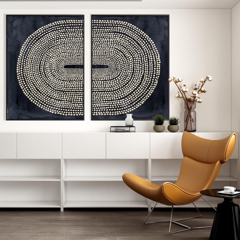 May include: Two abstract wall art pieces with a dark blue background and a pattern of white dots arranged in concentric circles. A modern, tan leather chair and a black side table complete the room's decor.
