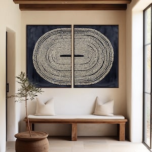 May include: Two abstract wall art pieces with a dark blue background and a white dotted oval design. The art hangs above a wooden bench with cream-colored pillows. A small tree in a woven pot sits nearby.
