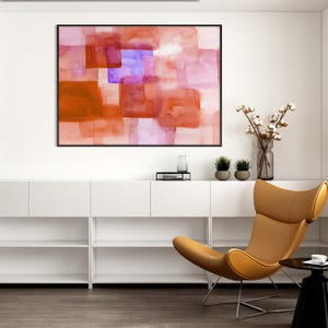 Peut inclure: Peinture abstraite &agrave; l'aquarelle dans un cadre noir. L'&oelig;uvre pr&eacute;sente des formes rectangulaires superpos&eacute;es dans des tons orange, rouge et violet. Int&eacute;rieur moderne et minimaliste avec une chaise en cuir beige et un meuble de rangement blanc.