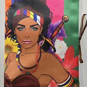 May include: A rectangular journal cover featuring a vibrant illustration of a person with dark curly hair, blue eyes, and a colorful headband. The design includes a sword, sunflowers, and red flowers against a striped background with brown ribbon ties.