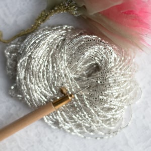 Op de afbeelding: Een close-up van een spoel met heldere, iriserende zaadkraaltjes met een houten kralen naald.