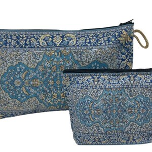 Puede incluir: Dos estuches con cremallera de color azul y dorado con borlas doradas. El estuche más grande está tumbado y el más pequeño está de pie.