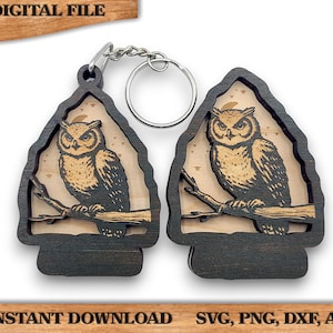 May include: A wooden owl keychain with a detailed carving of an owl perched on a branch with a crescent moon and stars in the background. The keychain is attached to a silver key ring.