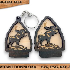 May include: Two wooden keychains featuring a moose silhouette within a mountain-shaped frame. The moose stands on a rocky base under a crescent moon and stars. The keychains are dark brown with a light wood interior. The words "DIGITAL FILE" and "INSTANT DOWNLOAD" are visible.