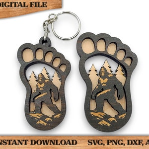 May include: A wooden keychain featuring a Bigfoot silhouette inside a footprint. The keychain is brown with a light brown interior and a silver key ring.