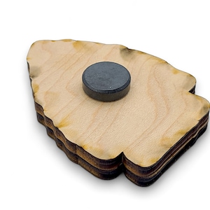 May include: A wooden cutout of a tree with a black magnet on the back. The tree is made of multiple layers of wood and has a rough, natural edge.