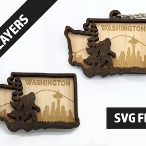 Puede incluir: Llaveros de madera de dos capas con la forma del estado de Washington. Los llaveros presentan una silueta de Bigfoot, el horizonte de Seattle y la palabra "WASHINGTON". Un llavero tiene un llavero plateado adjunto. También se ve el texto "2 LAYERS" y "SVG FILE".