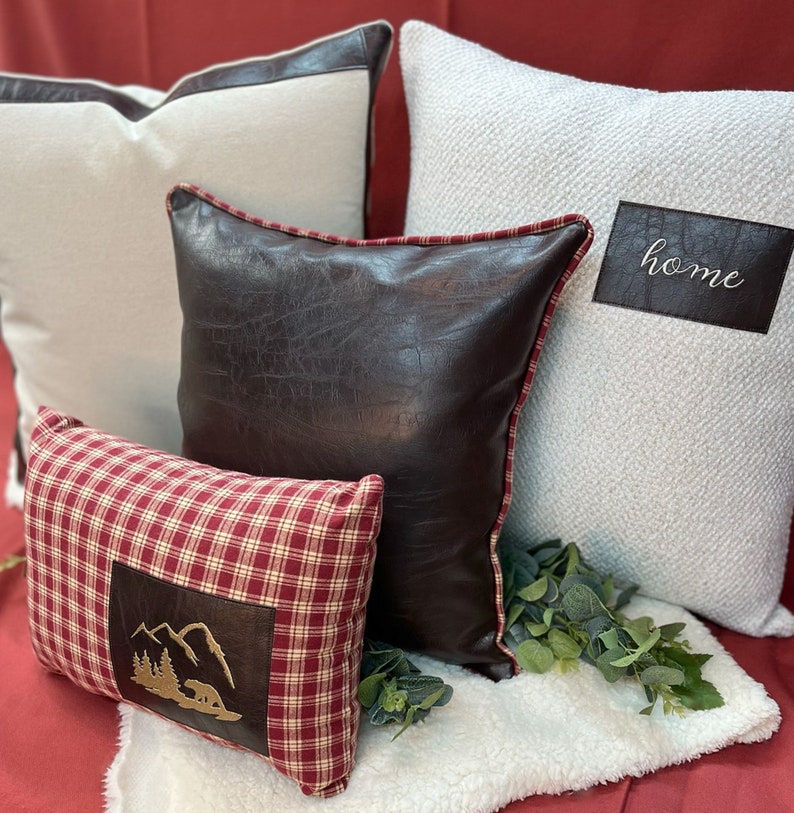 May include: Four decorative throw pillows on a white faux fur throw. The pillows are in various colors and textures, including red, white, brown, and black. One pillow has the word "home" embroidered on it.