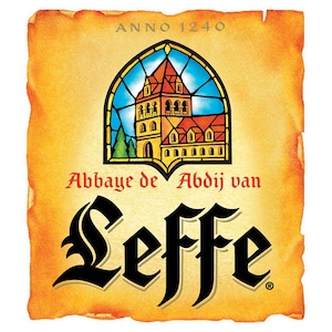 Puede incluir: Una etiqueta de estilo vintage con fondo de pergamino. Presenta una ilustración de vidriera de un edificio con tejado rojo y cielo azul. La palabra "Leffe" se muestra en una fuente estilizada, con "ANNO 1240" en la parte superior. También está el texto "Abbaye de Abdij van".