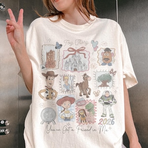 以下が含まれることがあります： クリーム色のTシャツ。トイ・ストーリーのキャラクターとイメージのコラージュが特徴です。ウッディ、バズ・ライトイヤーなどのイラスト、テキスト「Toy Story」と「You've Got a Friend in Me」が含まれています。