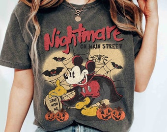 May include: A black t-shirt with a vintage-style graphic of Mickey Mouse dressed as a vampire. The graphic includes the text "Nightmare on Main Street" and a spider web with bats. The shirt also features a tombstone with the text "Stay with me."