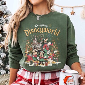 May include: Green sweatshirt featuring the text "Walt Disney Disneyworld 1971" with cartoon characters. The design includes Mickey Mouse, Minnie Mouse, Donald Duck, and Goofy. The sweatshirt is a crew neck style.