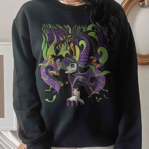 May include: A black crewneck sweatshirt featuring a graphic print of a purple and black dragon looming over a character with pale skin and a black headpiece, accompanied by a black bird and green flames, with small green bats scattered throughout.