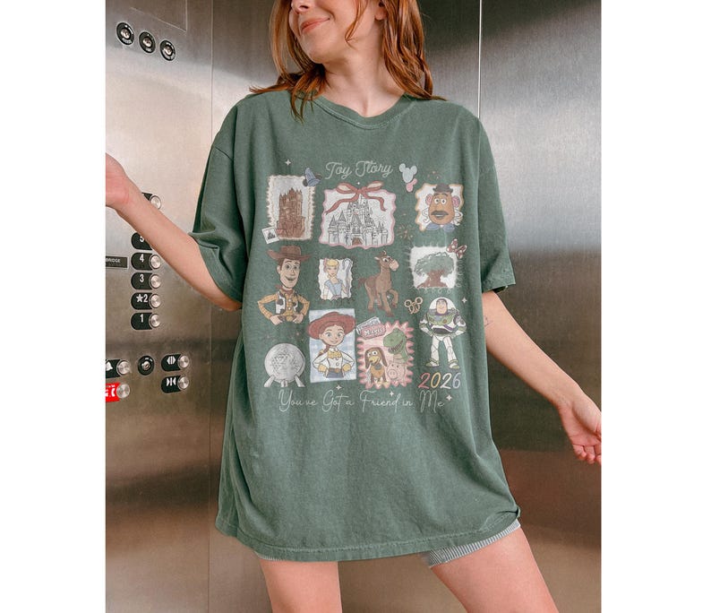 以下が含まれることがあります： トイ・ストーリーのコラージュデザインが施されたグリーンのTシャツ。映画の様々なキャラクターや画像、テキスト「Toy Story」、「You've Got a Friend in Me」、そして年号「2026」が特徴です。このTシャツはオーバーサイズです。