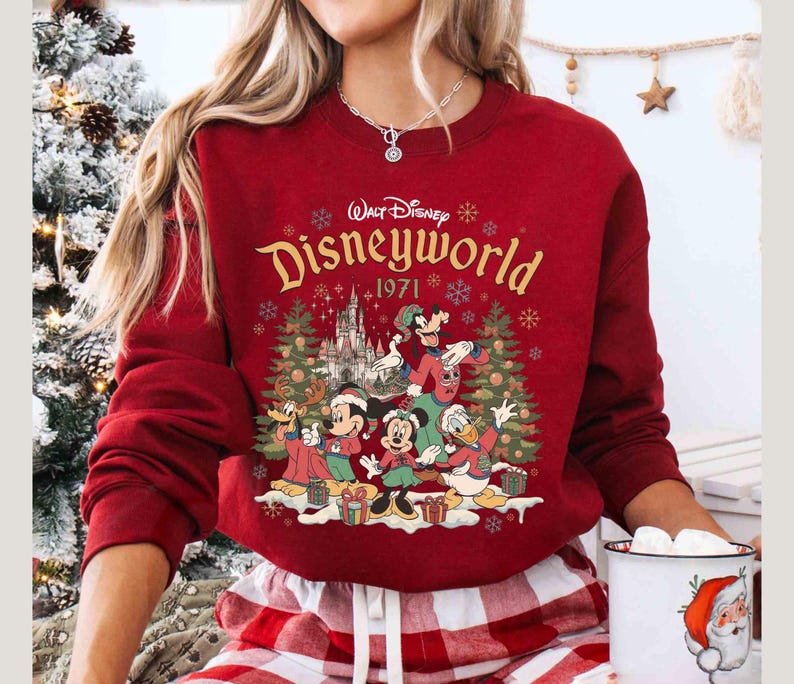 May include: A red sweatshirt featuring a Disney World graphic with Mickey Mouse, Minnie Mouse, Donald Duck, Goofy, and other characters. The graphic includes the text "Walt Disney Disneyworld 1971" and Christmas trees.