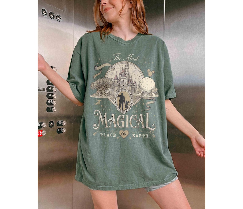 May include: A green t-shirt with the text "The Most Magical Place on Earth" in a vintage style. The graphic includes a castle, a tree, and a silhouette of a person. The shirt is oversized and has short sleeves.