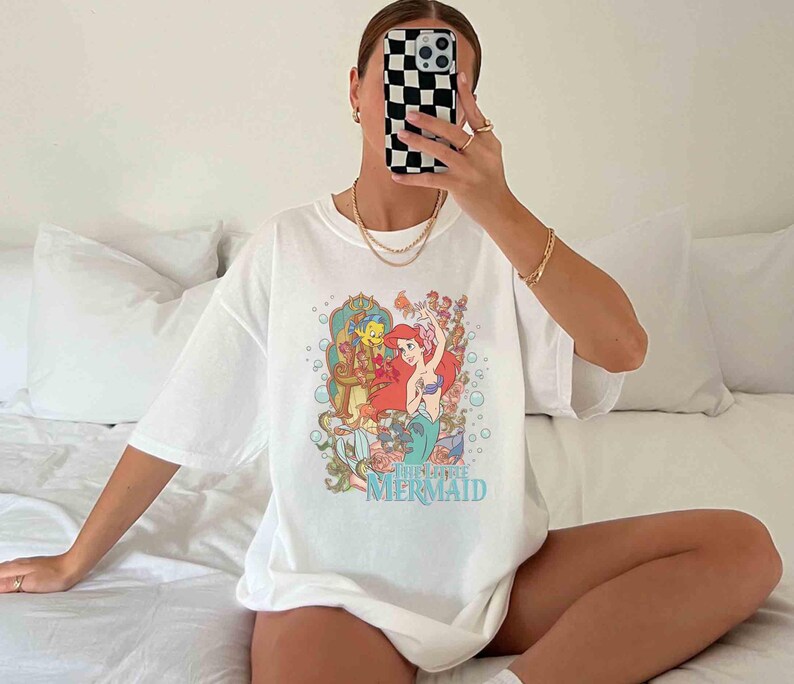 May include: White t-shirt featuring a graphic print of Ariel, the Little Mermaid, with Flounder and Sebastian. The text "The Little Mermaid" is printed below the image.