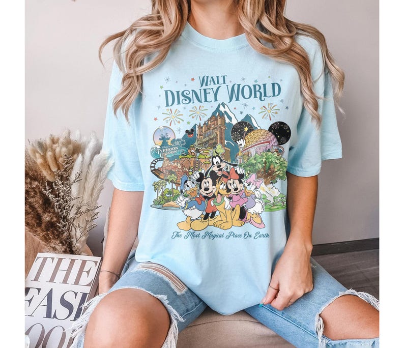 May include: Pale blue t-shirt with a graphic of Disney characters and attractions, including the text "Walt Disney World" and "The Most Magical Place on Earth". The shirt has a crew neck and short sleeves.