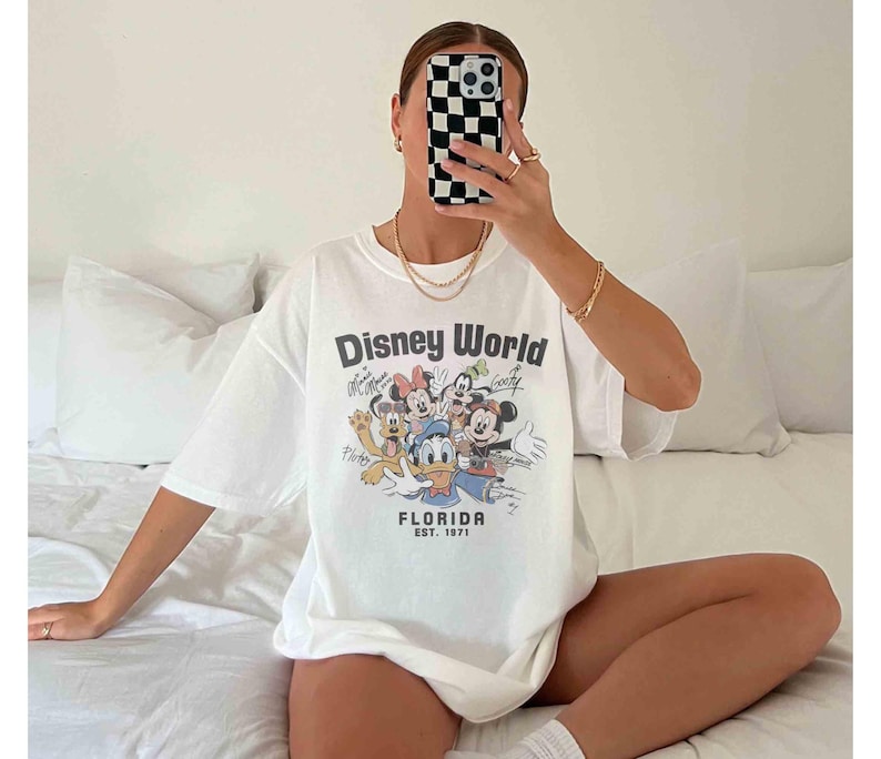 May include: White t-shirt featuring a Disney World graphic with Mickey Mouse, Minnie Mouse, Donald Duck, and other characters. The shirt includes the text "Florida Est. 1971" in a vintage style.