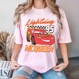 Peut inclure: T-shirt rose avec une image de dessin anim&eacute; de Flash McQueen du film Cars. Le t-shirt porte l'inscription "Lightning 95 McQueen".