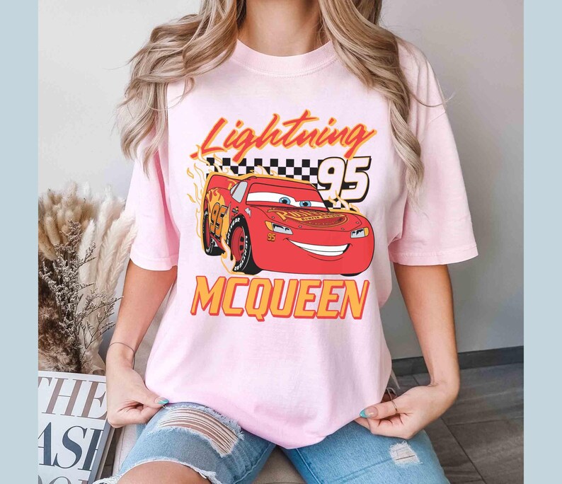 Peut inclure: T-shirt rose avec une image de dessin anim&eacute; de Flash McQueen du film Cars. Le t-shirt porte l'inscription "Lightning 95 McQueen".