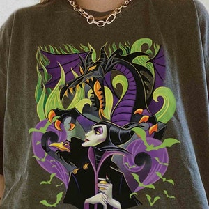 May include: A charcoal gray t-shirt featuring a graphic print of a dark-haired character in a black robe, a large purple and black dragon, a black bird, and green bats. The design includes swirling green and purple smoke elements.