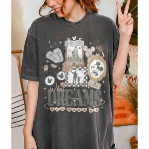 K&ouml;nnte beinhalten: Dunkelgraues T-Shirt mit einem skurrilen Design mit einem Schloss, Mickey Mouse und dem Text "What Dreams are Made Of". Das Design hat Disney-Elemente. Das T-Shirt hat eine lockere Passform.