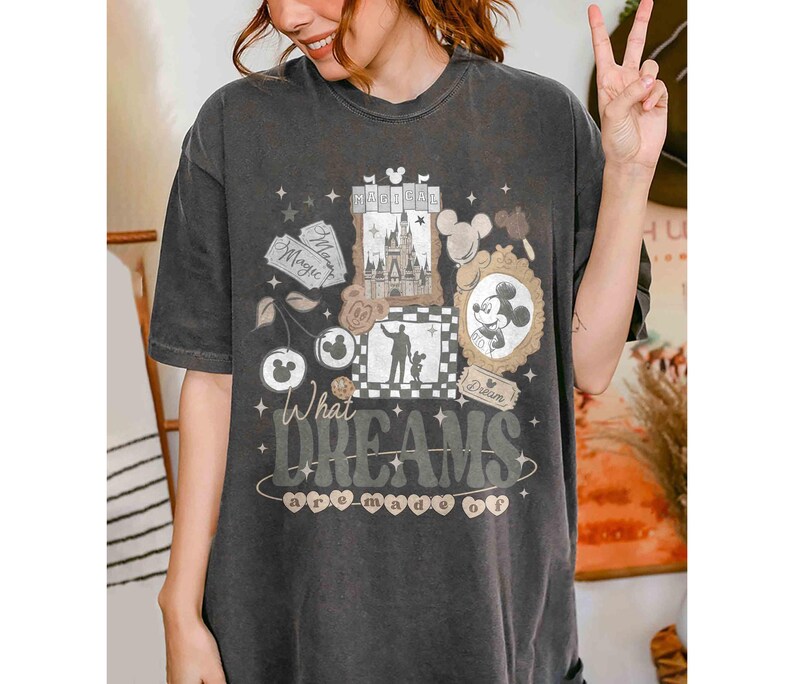 K&ouml;nnte beinhalten: Dunkelgraues T-Shirt mit einem skurrilen Design mit einem Schloss, Mickey Mouse und dem Text "What Dreams are Made Of". Das Design hat Disney-Elemente. Das T-Shirt hat eine lockere Passform.