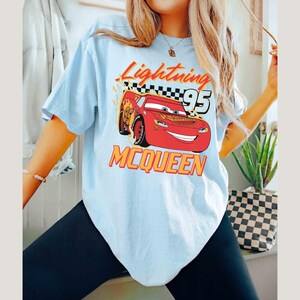Peut inclure: Un t-shirt bleu clair avec un imprim&eacute; de Flash McQueen du film Cars de Disney Pixar. L'imprim&eacute; comprend le texte "Lightning McQueen 95".