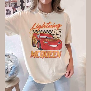 Peut inclure: Un t-shirt blanc avec une image de dessin anim&eacute; de Flash McQueen du film Cars de Disney Pixar. Le t-shirt porte l'inscription "Lightning 95 McQueen".