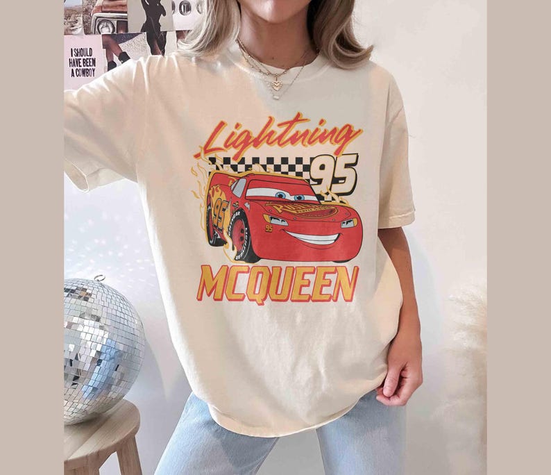 Peut inclure: Un t-shirt blanc avec une image de dessin anim&eacute; de Flash McQueen du film Cars de Disney Pixar. Le t-shirt porte l'inscription "Lightning 95 McQueen".