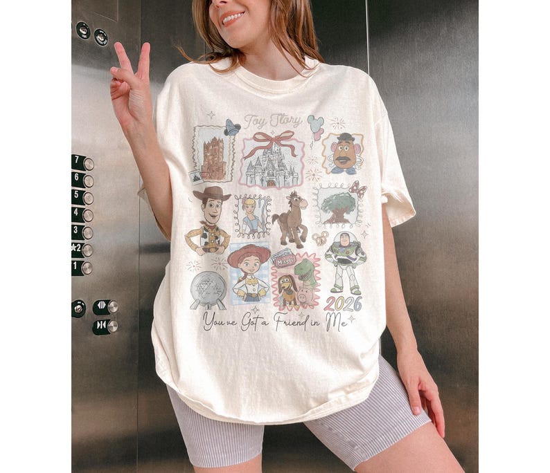 以下が含まれることがあります： クリーム色のTシャツ。トイ・ストーリーのキャラクターとイメージのコラージュが特徴です。ウッディ、バズ・ライトイヤーなどのイラスト、テキスト「Toy Story」と「You've Got a Friend in Me」が含まれています。