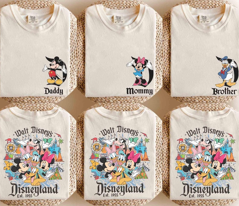 以下が含まれることがあります： ディズニーのキャラクターのグラフィックがプリントされたクリーム色のTシャツ6枚セット。Tシャツには、ミッキーマウス、ミニーマウス、ドナルドダック、そしてディズニーランドパークのシーンの前にいるディズニーキャラクターのグループが描かれています。Tシャツには、「パパ」、「ママ」、「ブラザー」、「ウォルトディズニーのディズニーランドEst. 1955」という文字がプリントされています。