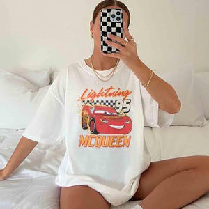 Peut inclure: T-shirt blanc avec un dessin de voiture de course rouge et le texte "Lightning McQueen 95".