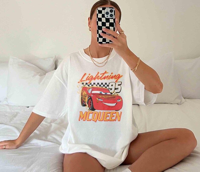 Peut inclure: T-shirt blanc avec un dessin de voiture de course rouge et le texte "Lightning McQueen 95".