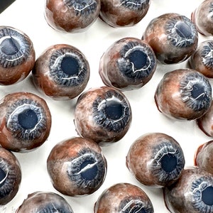 May include: A collection of realistic eyeball-shaped candies, each with a brown outer layer and a blue iris. The candies are arranged on a white surface.