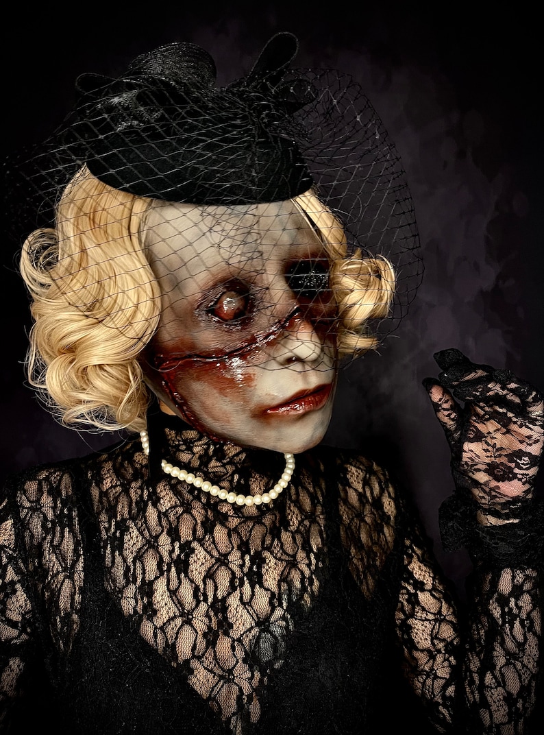 May include: A woman wearing a black lace dress and a black hat with a veil. Her face is covered in white and red makeup, creating a spooky and eerie look.