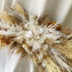 May include: A dried floral arrangement with white silk flowers and pampas grass in shades of beige and brown.